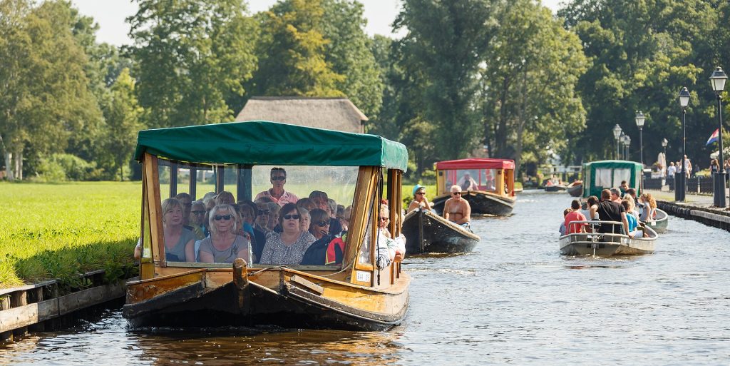 Matkailijoita veneellä Giethoornin kanavalla olkikattoisten talojen keskellä