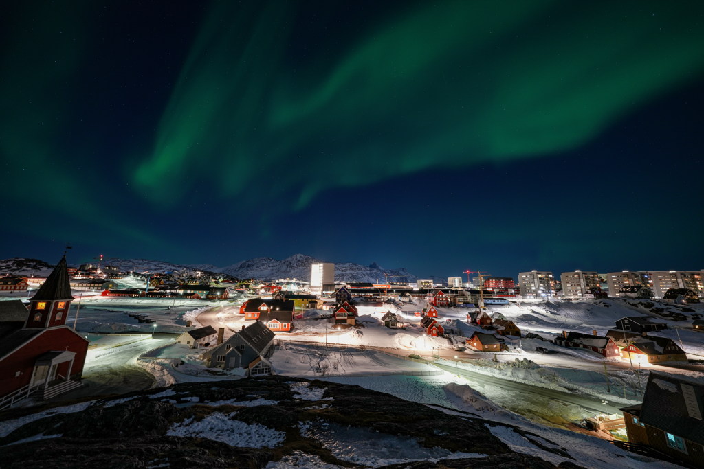 Vihreät revontulet Nuukin valaistun kaupungin yllä talviyönä