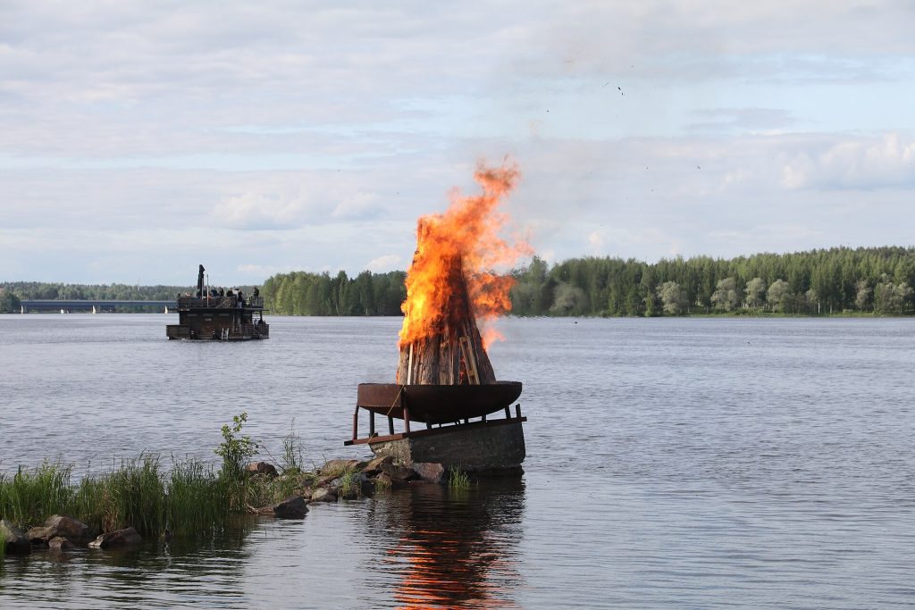 Lautalle rakennettu juhannuskokko palaa järvellä, taustalla metsäinen ranta