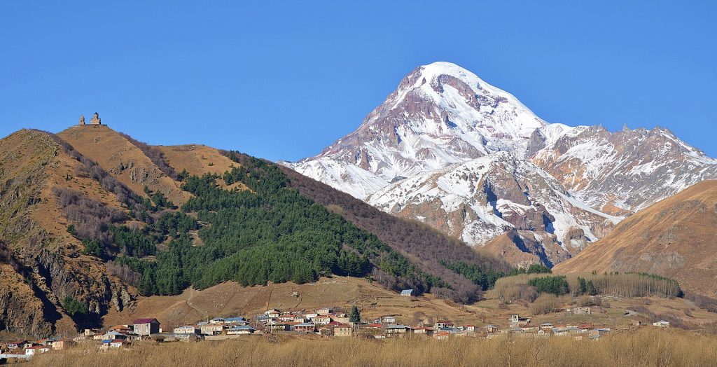 Lumihuippuinen Kazbek-vuori ja Gergetin kolminaisuuden kirkko vihreällä kukkulalla