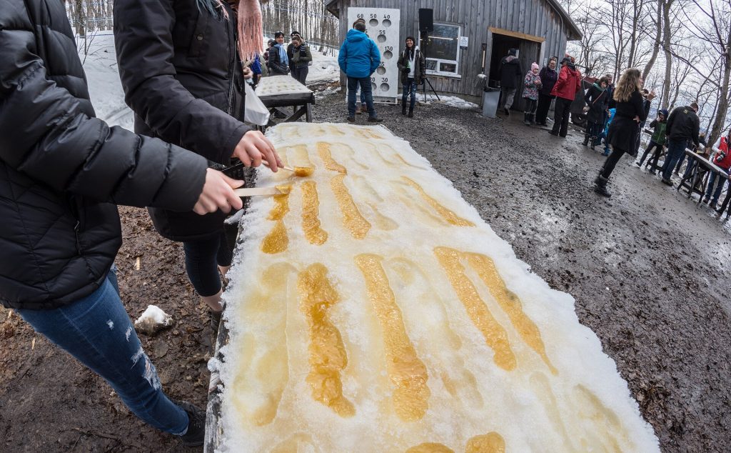 Kuumaa vaahterasiirappia valetaan lumen päälle toffeeksi sokerimajan pihalla Québecissä
