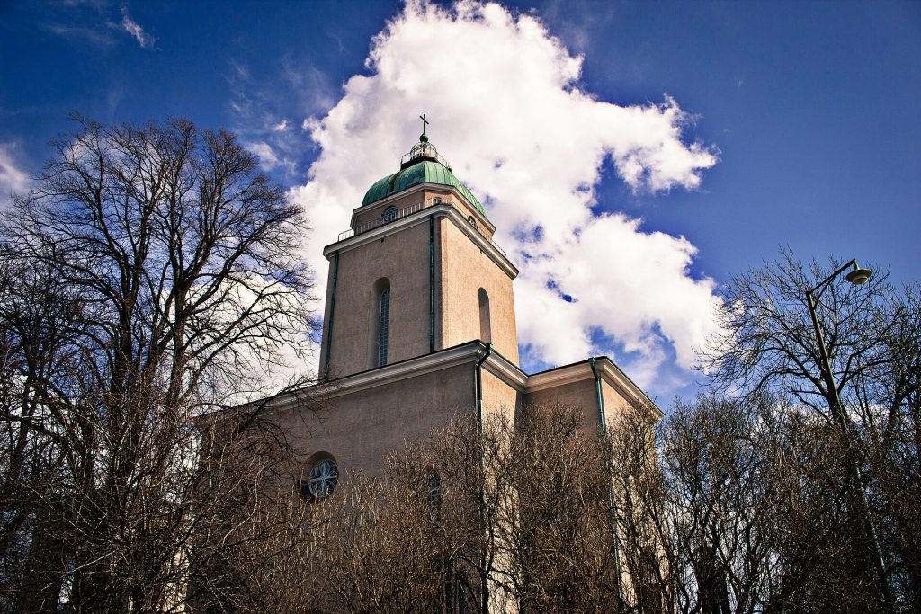Suomenlinnan kirkon vaalea torni ja kupoli puiden takaa sinistä taivasta vasten